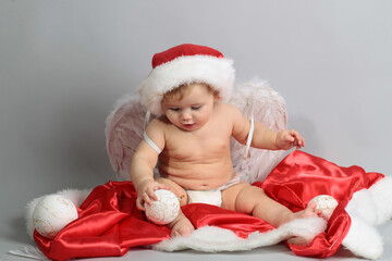 Happy baby in a Christmas costume and Santa hat with wings.