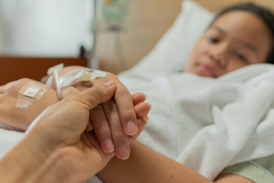 Young patient asian woman lying on bed, focus hand holding hand of sick kid and mother on bed were connected to saline solution in hospital. Selective focus, healthcare and health insurance concept.