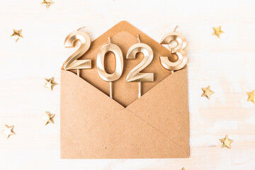 An open kraft envelope on a white wooden table with numbers 2023 in gold color. Christmas and New...