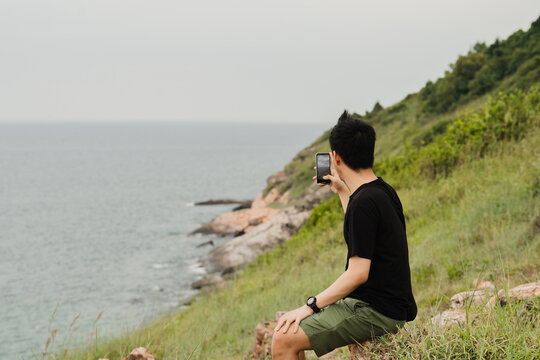 A picture of a man sitting and taking pictures of mountain landscapes and sea views.