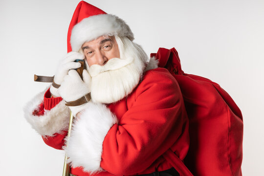 Equipped Santa Claus with a bag of gifts traveled on skis. In the foreground, looking at the camera. Active image of Santa on white background photo studio.