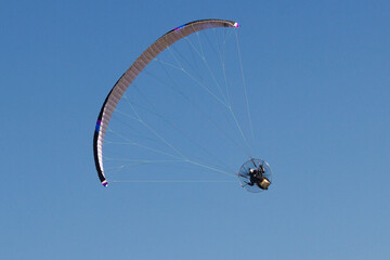 Person riding a paraglider against the blue sky in the background