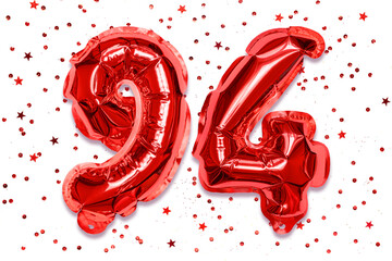 The number of the balloon made of red foil, the number ninety-four on a white background with sequins. Birthday greeting card with inscription 94. Numerical digit. Celebration event.