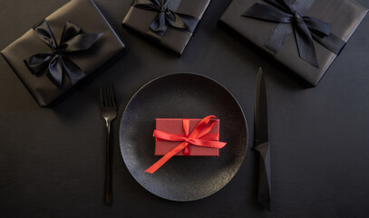 Gift black box, plate with fork and knife on a black background. Creative table setting. Holiday concept. Place for text or advertising. Christmas. Valentine's Day.
