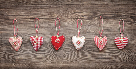 Fototapeta premium six hand-sewn fabric hearts hang on a string in front of a wooden board. rustic decoration concept
