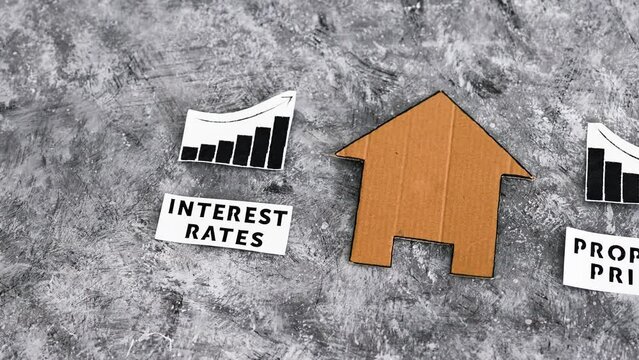 interest rates increasing and property prices dropping, cardboard house in between graphs with stats going in opposite directions