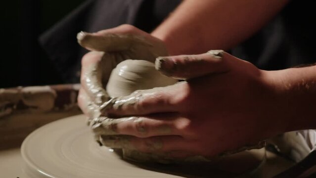 A man forms wet clay on a potter wheel