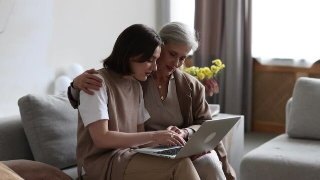 adult daughter explaining to elderly mother how to use laptop and modern gadgets