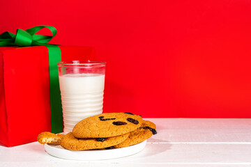 Hand of Santa Claus with traditional Christmas cookie snack with milk glass. Santa Dunking Cookie, on bright festive red and white wooden  background. Merry Christmas and Happy New Year greeting card