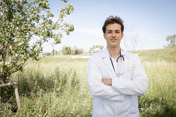 jonge sympathieke dokter met witte jas en stethoscoop om zijn nek staat buiten voor groene weide