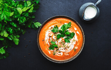 Hot spicy pumpkin soup puree with pumpkin seeds, cream, pepper and parsley. Winter or autumn healthy vegan vegetarian food. Soup bowl on black table background. Top view