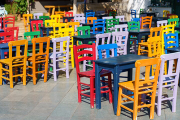 Fototapeta na wymiar Street cafe in summer with color wooden vintage chairs and tables on a tourist street. Colored furniture and cafe design