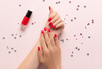 Female hands with trendy red manicure on pink background with confetti. Party, festive, holidays or celebration vibes - obrazy, fototapety, plakaty