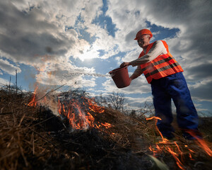 Firefighter ecologist fighting fire in field with cloudy sky on background. Male environmentalist...