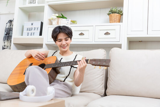 Playful asian woman playing acoustic guitar music instrument at home, young Asian musician girl lifestyle