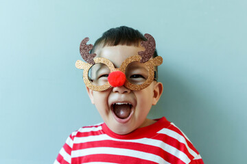 Excited Little Asian child boy in Christmas reindeer glasses on blue isolated background.