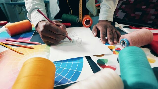 African dressmaker is sketching a dress on his desk