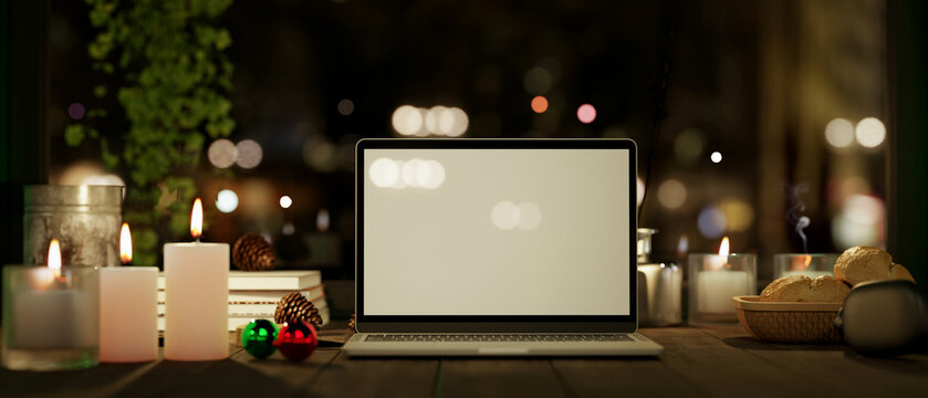 Workspace at night with laptop mockup with candles on wood table over blurred dark background.