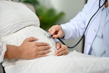 Female doctor or obstetrician listening baby's heartbeat by her stethoscope. Antenatal care