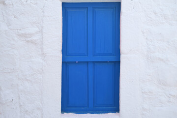 Bright blue door on white wall of historic building, window with closed shutters