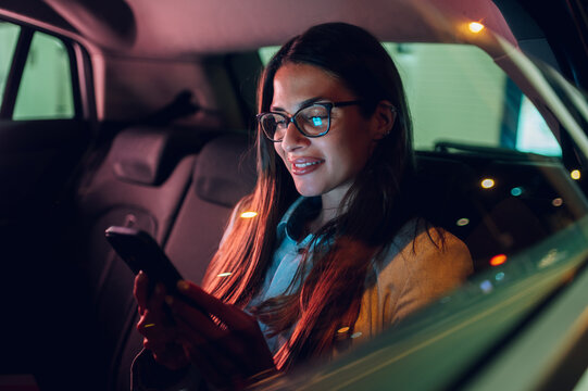 Business woman using smartphone while sitting in a backseat of a car at night