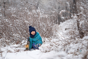 Fototapeta na wymiar A little boy plays with the snow, rejoices in the snow and carries his flashlight through the forest to Santa Claus.