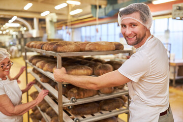 Bäcker schiebt Tablettwagen mit frisch gebackenen Broten