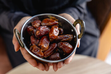 Young woman's hand offering dried dates in a cup