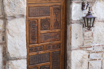 Old wooden door with an ornament and a carved lantern on the wall of the house