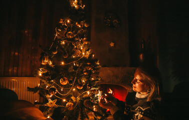 Woman Decorating the Christmas tree with golden decorations on it next to the fireplace. Christmas Eve concept. 
