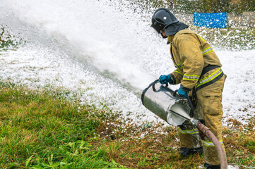 A firefighter in protective clothing extinguishes the fire by feeding foam. A firefighter extinguishes a fire with a foam generator. Extinguishing a fire in a tank farm with flammable liquids.