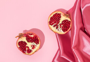 Romantic creative layout with pomegranate halfs and pink satin fabric on pink background. Fashion...