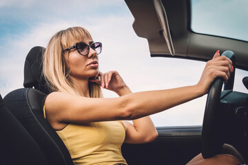 Young cute girl preens while driving. blonde admires herself in mirror.