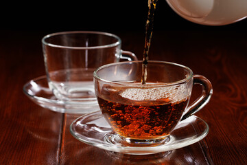 Hot tea is poured into a glass cup from a teapot. Selective focus.