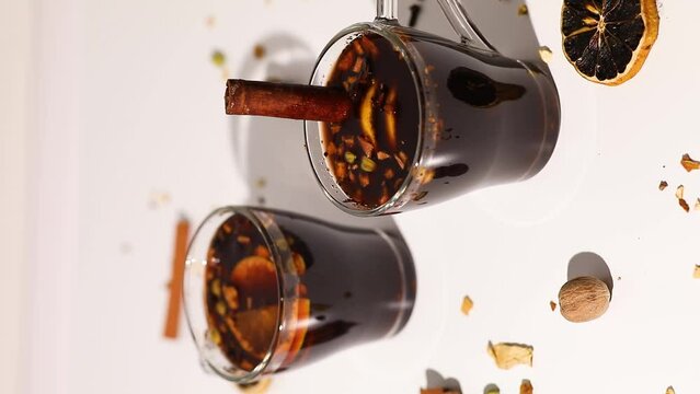 Vertical video woman hand put cinnamon stick on cup with Christmas mulled red wine with spices and oranges on a white background hard light, traditional hot drink at Christmas, festive cocktail