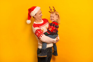 Happy smiling family father and daughter wearing Christmas sweaters, Santa Claus hat, reindeer antlers headwear and laughing on yellow background.

Young man and little girl celebrating New Year.