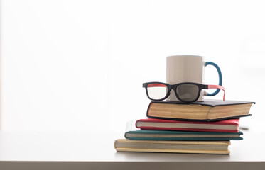 Hot coffee or tea, cocoa, chocolate cup on book and eyeglasses with copy space for text against the background of a bookshelf. Pile of books, glasses and cup on a table in the library.