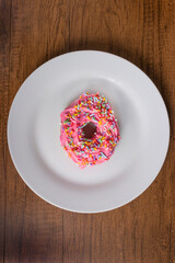 Tasty sweet donuts with pink frosting and colorful sprinkles served on a white plate. Candy top view photography.