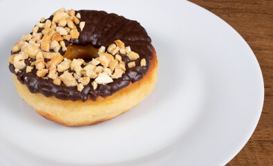 Sweet donuts with chocolate icing and nuts served on a white plate. Close-up photography with empty space for texts and additions.