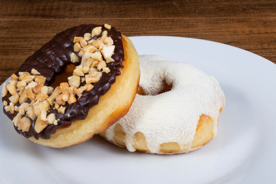 Sweet donuts with cream and powdered milk frosting and another donuts with chocolate and chestnut frosting and walnuts close-up photo.