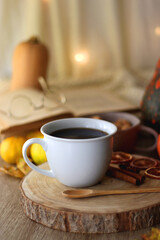 Cup of tea or coffee, seasonal spices, bowl of cookies, blanket, pumpkins, colorful leaves, books and tangerines on wooden table. Cozy hygge at home. Selective focus.