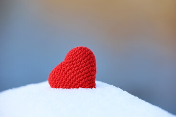 Red knitted heart in the snow on blurred background. Symbol of romantic love, Valentine's card