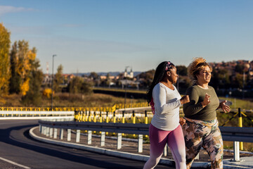 Two young plus size women jogging together on road.