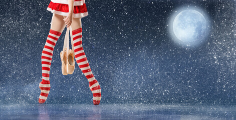 Legs of a ballerina on pointe shoes in striped golfs of Santa Claus walks against the backdrop of a...