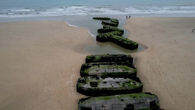People standing on Normandy Beach next to World War 2 bunker ruins