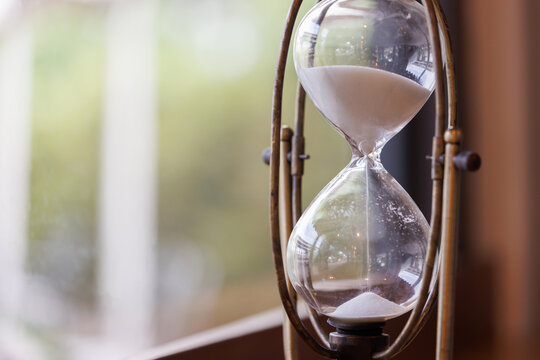 white sand hourglass near the window with gardeb background. close up vintage timer clock.