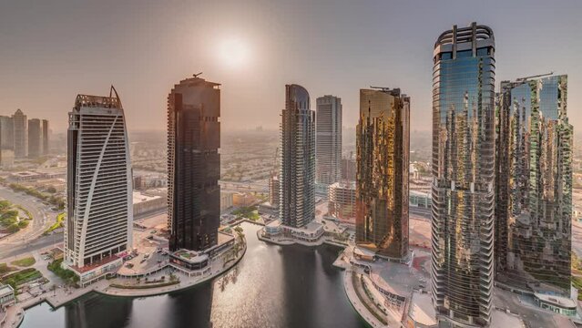 Sunrise over tall residential buildings at JLT district aerial timelapse, part of the Dubai multi commodities centre mixed-use district. Skyscrapers around pond