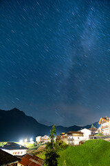 A small star trail with milky way visible above a small town in alps, Sauris, Italy