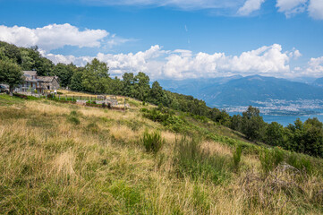 Fototapeta na wymiar Mountain landscape with stone houses, blue sky and clouds with Lake Maggiore in the background