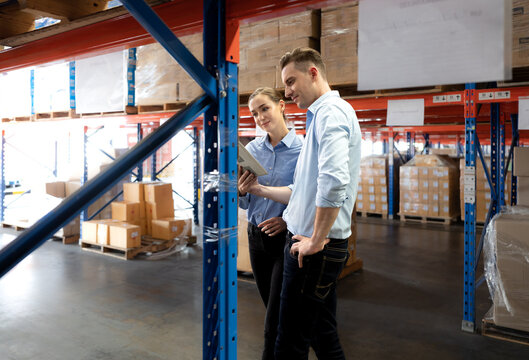 Distribution warehouse manager and client businesswoman using digital tablet checking inventory storage on shelf. Storehouse supervisor worker and logistic engineer standing together at storage room.